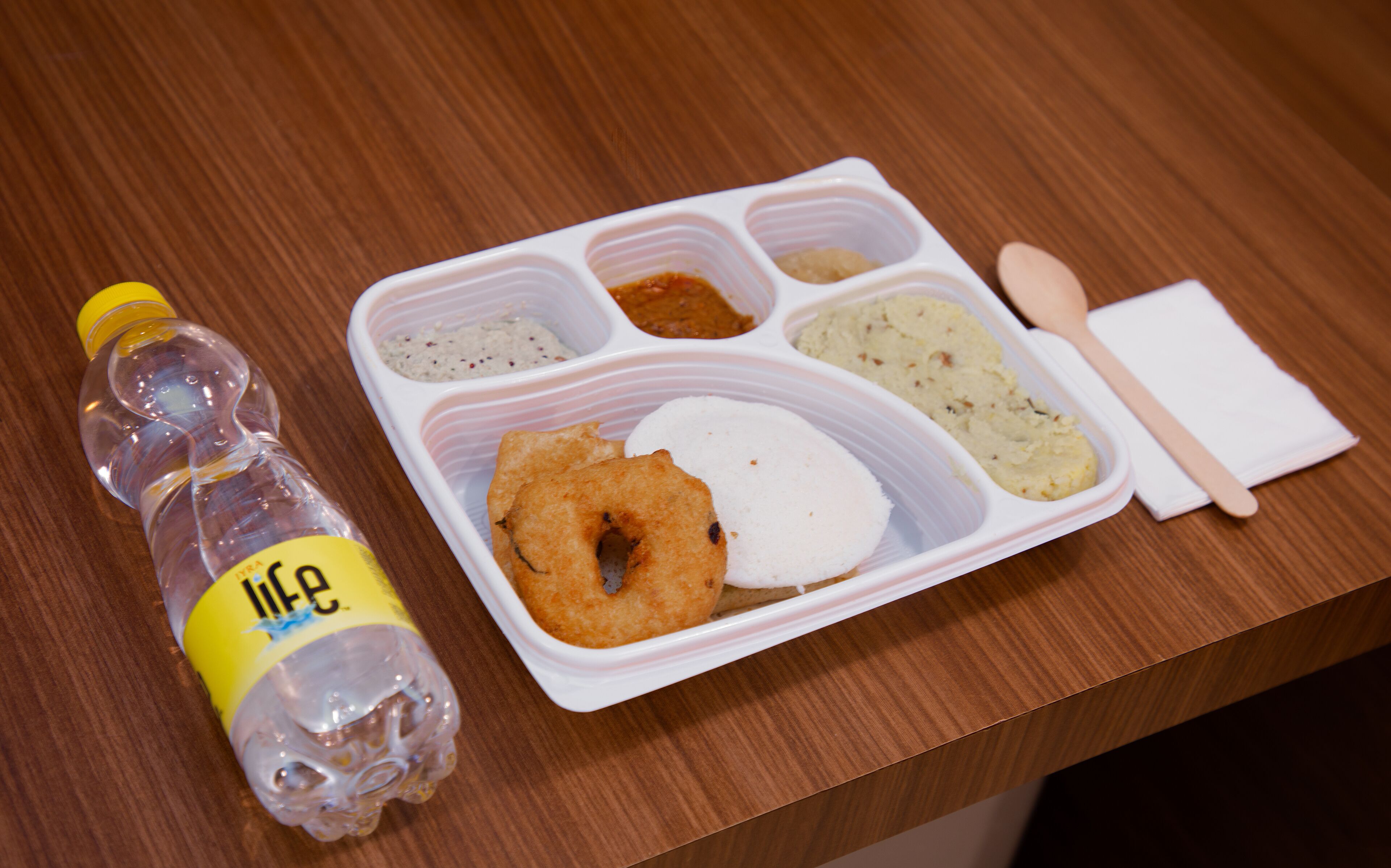Een plastic waterfles met een geel etiket en een witte plastic bak met vakken voor etenswaren.