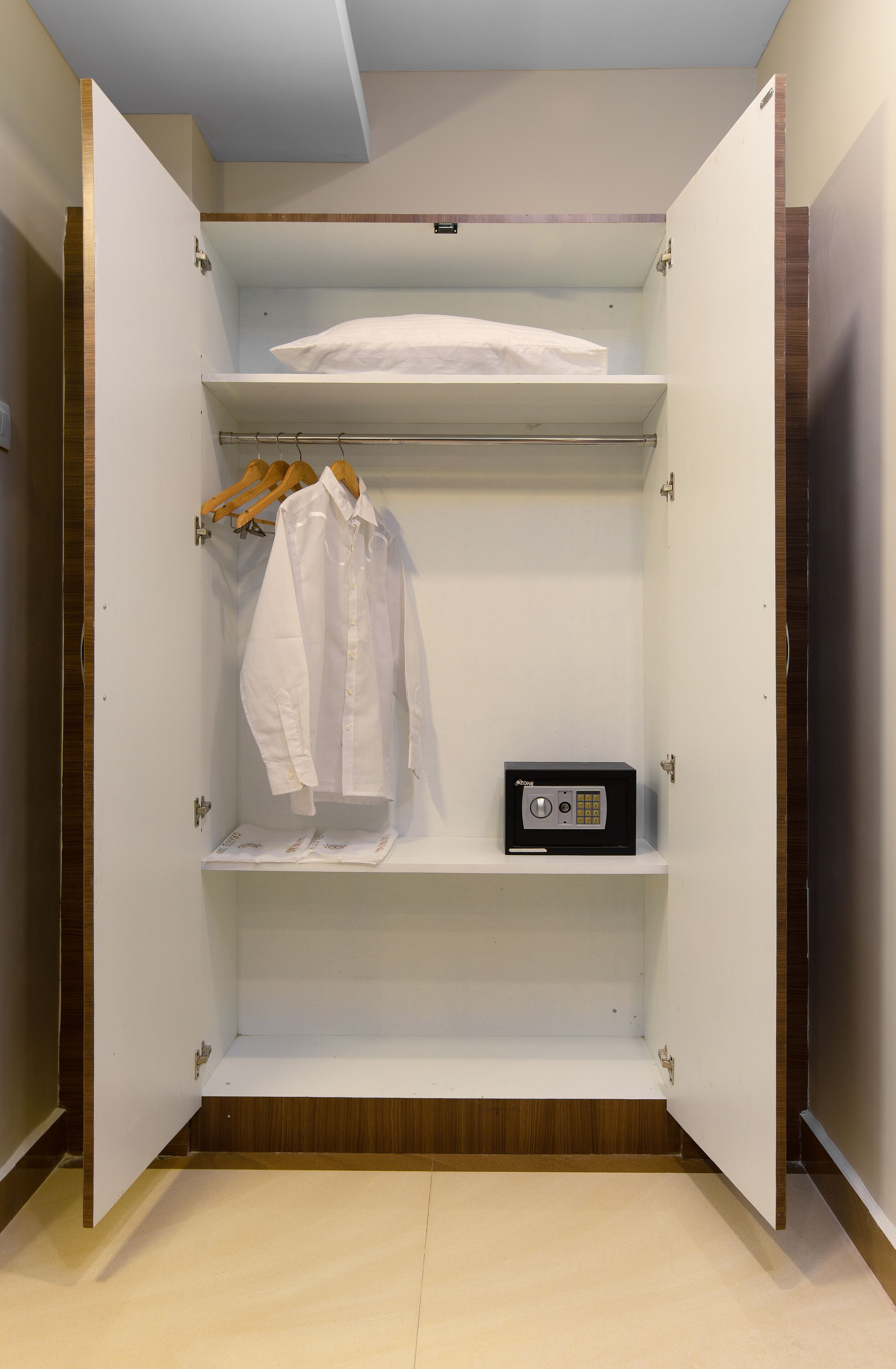 Armadio a muro con ante aperte, dotato di una rastrelliera per appendere i vestiti, uno scaffale con una camicia bianca e un piccolo dispositivo elettronico.