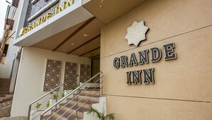 Exterior do Grande Inn, com uma escadaria que leva à entrada, uma parede decorativa e uma placa.