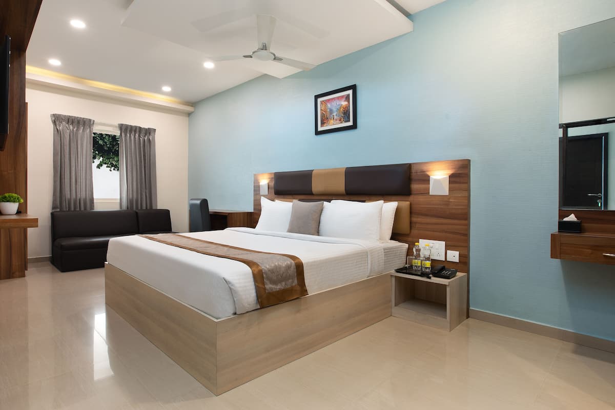 A modern hotel room with a large bed, a desk, a chair, a TV, and a window with curtains.