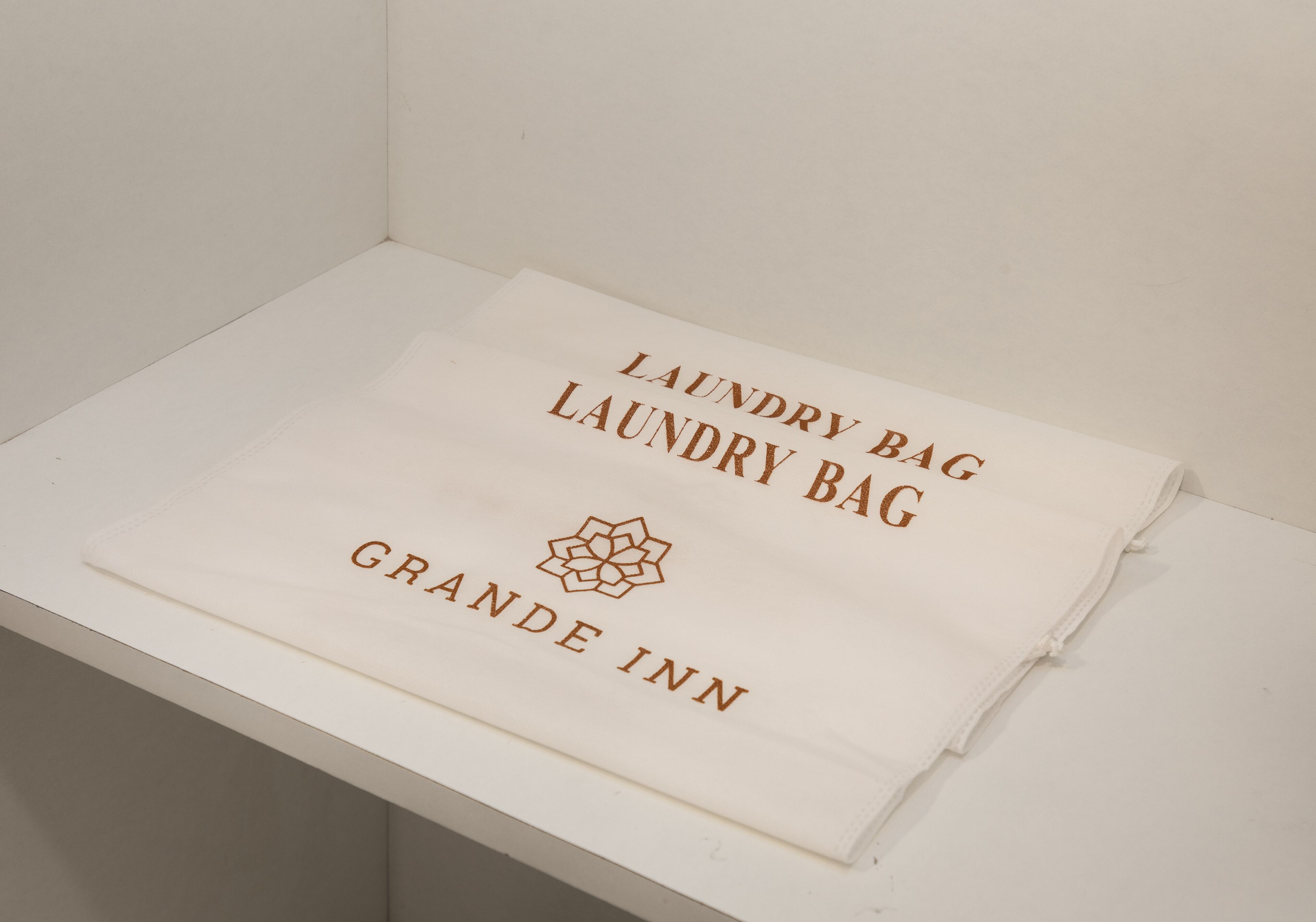 A folded white towel with the text "Laundry Bag Laundry Bag Grande Inn" and a logo.