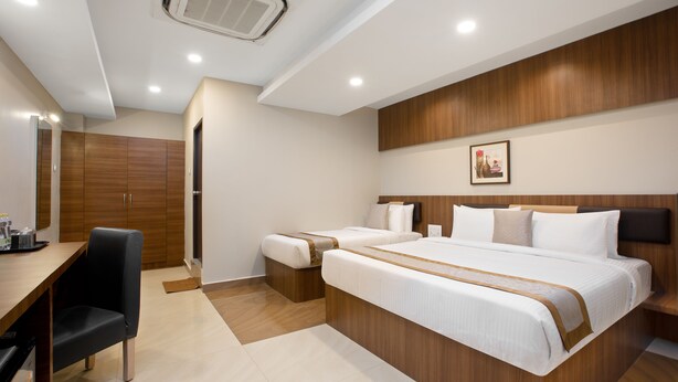Quarto de hotel moderno com cabeceira de madeira, duas camas, uma escrivaninha e uma cadeira.