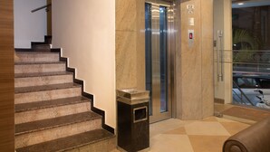 Um hall de hotel com escadaria de mármore, elevador e área de recepção.