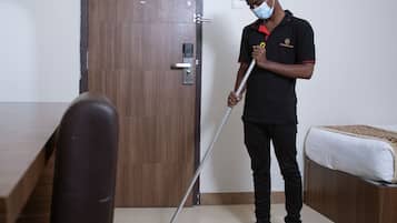 A hotel room with a wooden door, a bed with a white mattress, and a person mopping the floor.