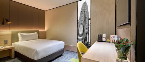 Ein Hotelzimmer mit Bett, Schreibtisch, Stuhl, Blumenvase und Blick auf ein hohes Gebäude.