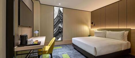 Una camera d'albergo con un letto, una scrivania con una sedia, una televisione a schermo piatto e vista su un edificio attraverso una finestra.