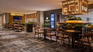 A modern lounge area with wooden furniture, a bar, and a television screen displaying a program. - Aerotel Kuala Lumpur (Sepang)
