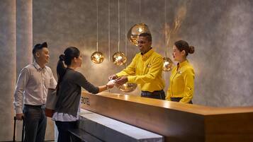 Un espace d’accueil d’hôtel au design moderne, comprenant un comptoir d’accueil, des luminaires suspendus et un mur aux couleurs neutres.