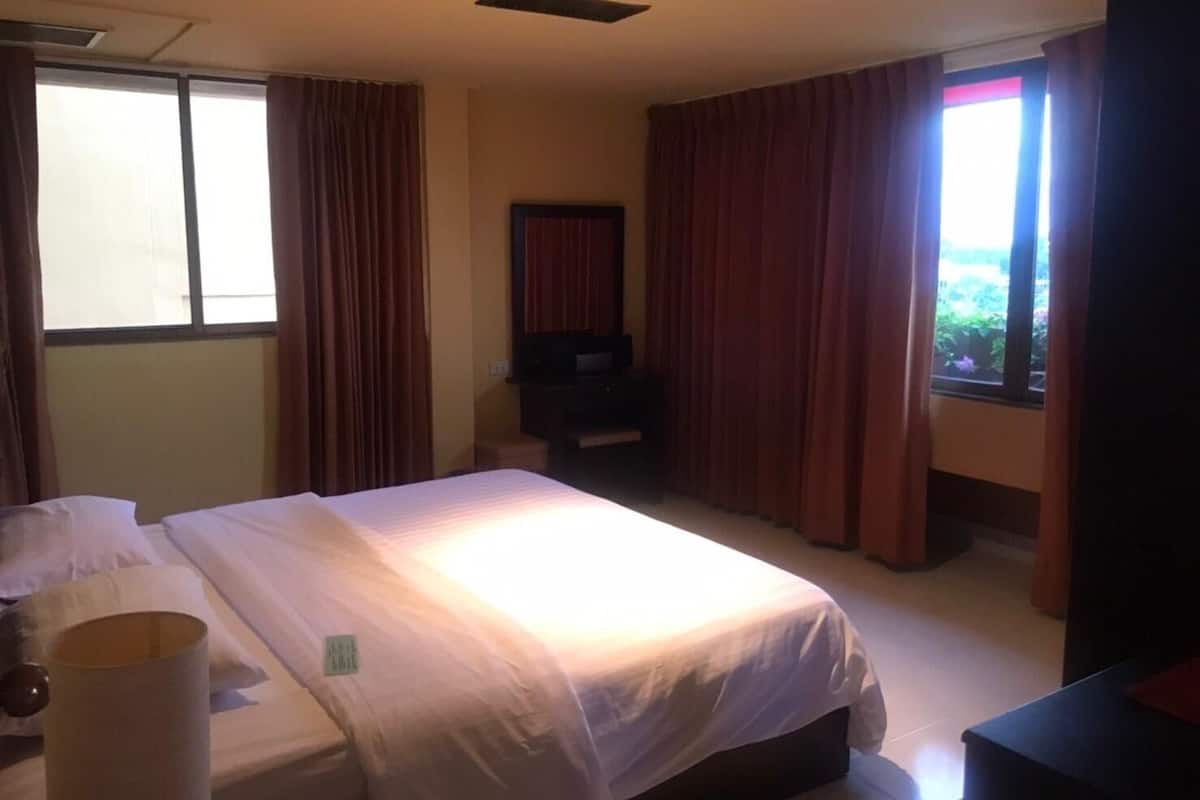 A hotel room with a bed, a TV, a window with curtains, and a view of greenery outside.