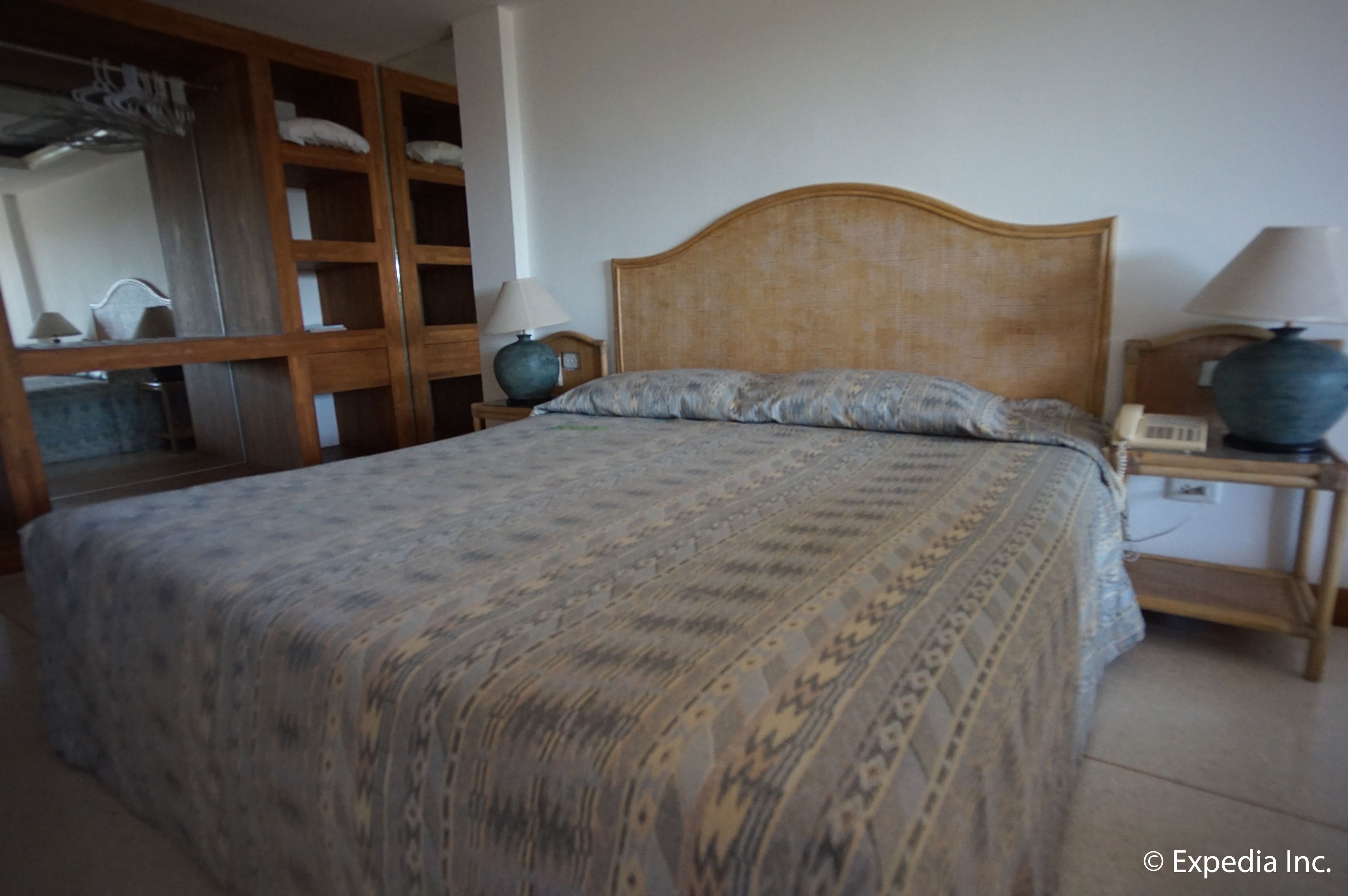 Una camera da letto con un letto grande, una testiera in legno, due comodini con lampade, un armadio con ante a specchio e un piccolo comodino con il telefono.