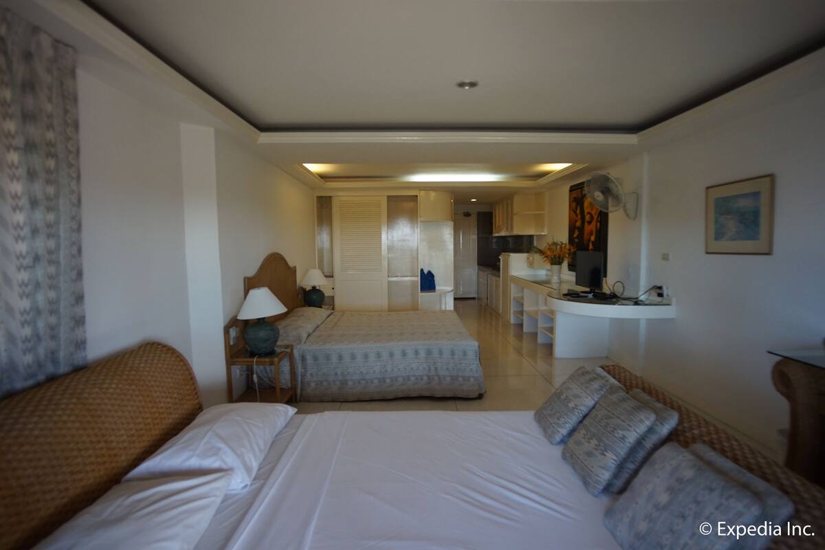 A hotel room with two beds, a desk, a chair, and a kitchenette.