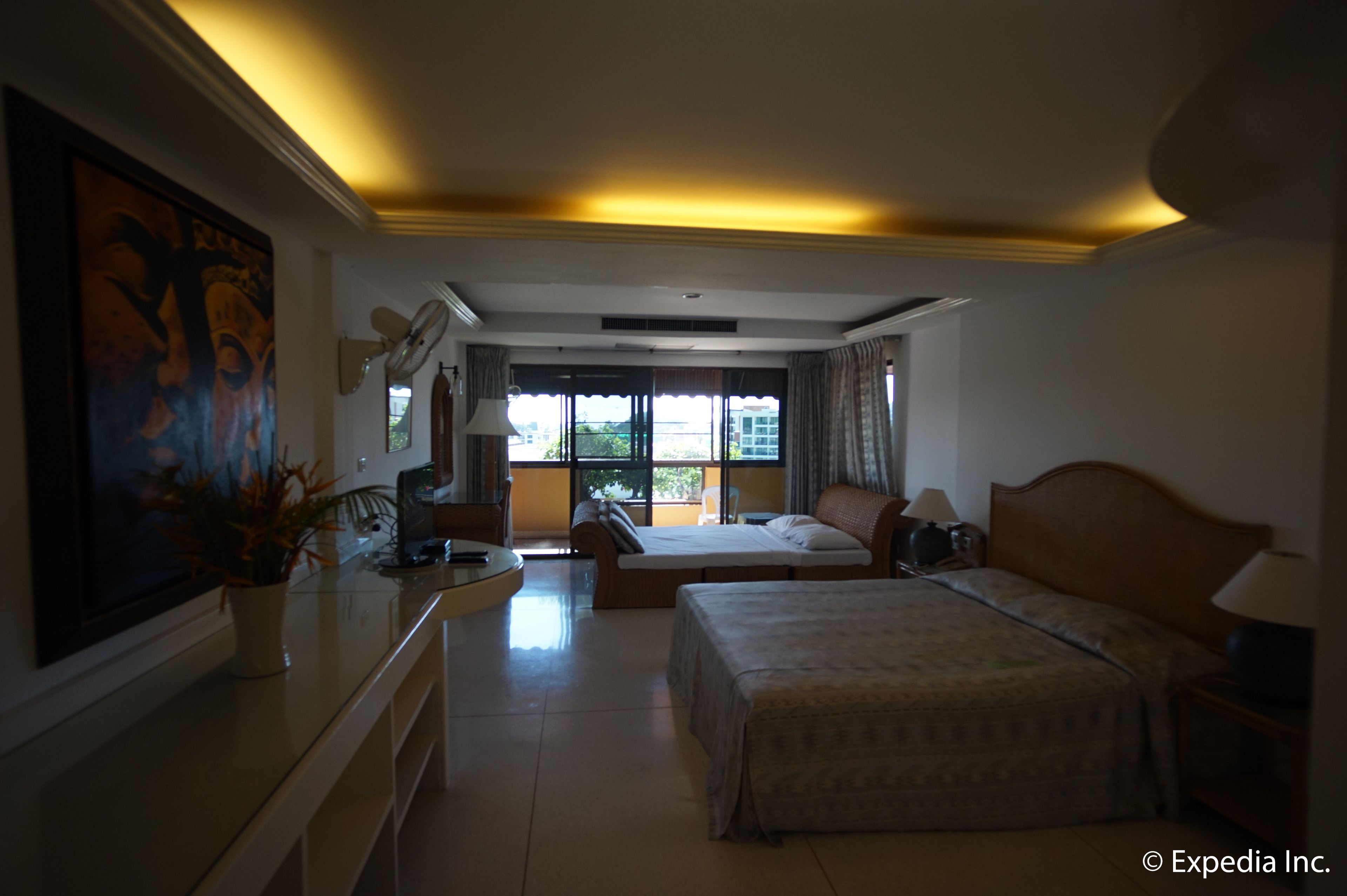 Une chambre d’hôtel comprenant un lit, des tables de chevet, un bureau, une chaise, une fenêtre avec des rideaux, un ventilateur de plafond et un tableau au mur.