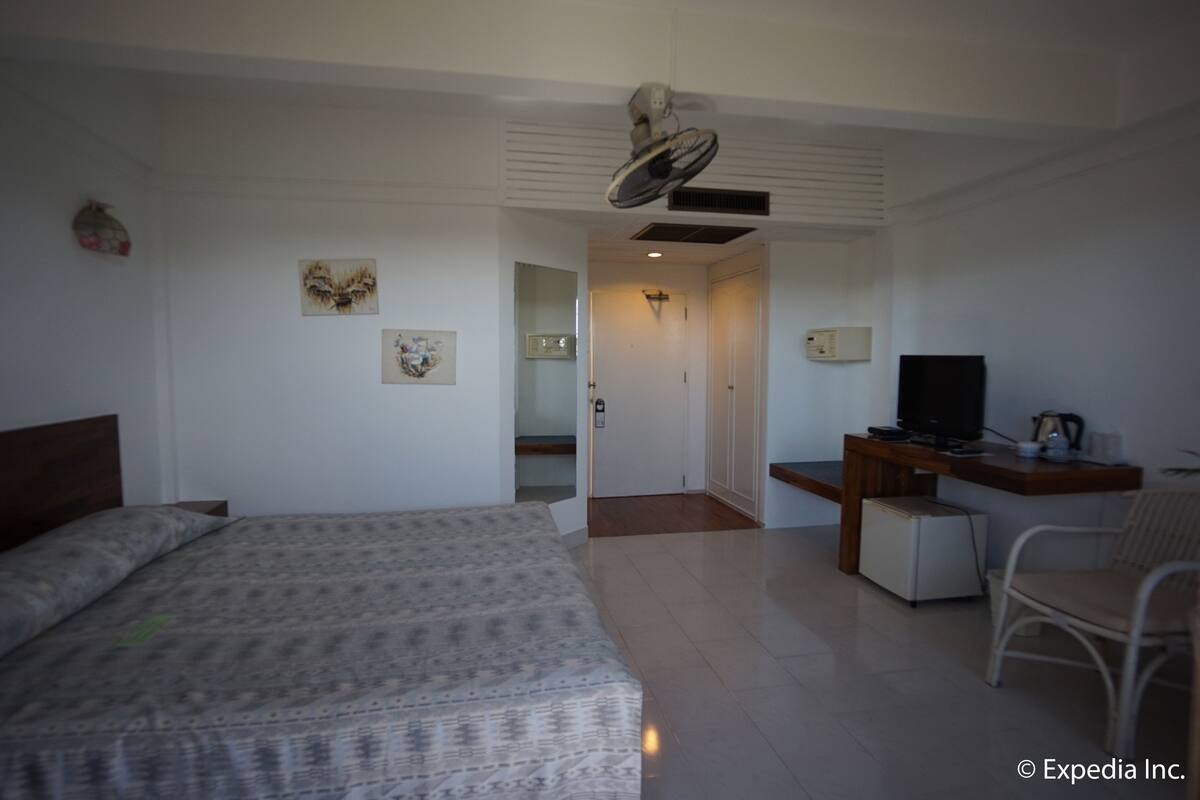 A hotel room with a bed, a desk with a television, a chair, and a small refrigerator.