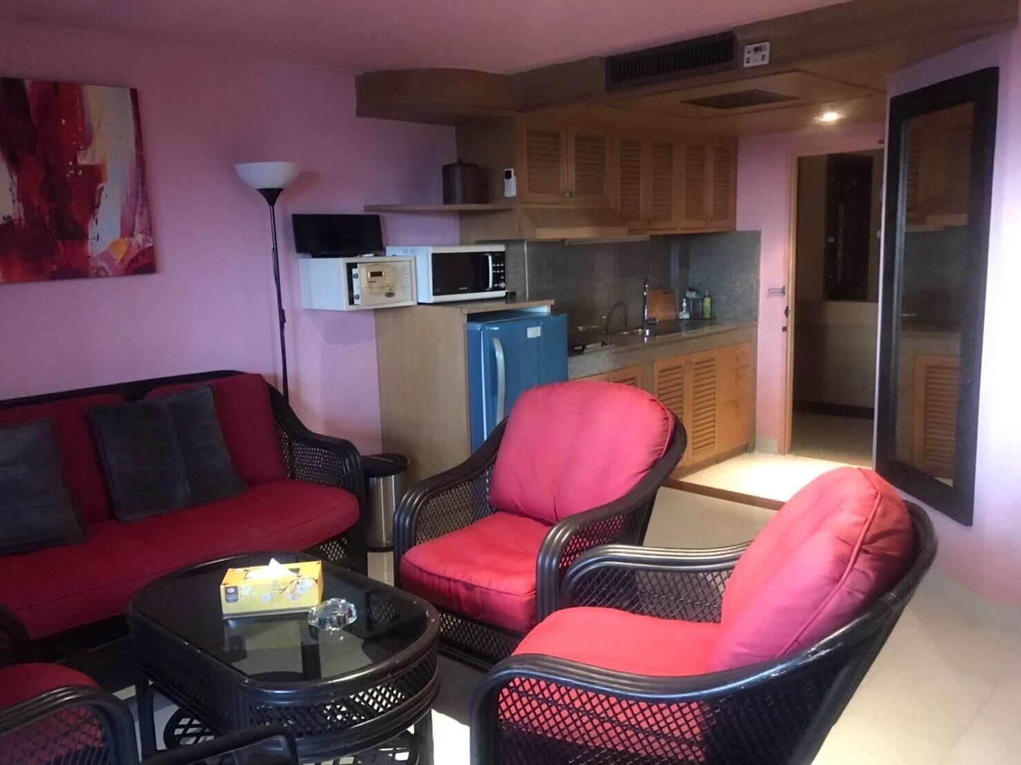 Ein gemütlicher Wohnraum mit Küchenzeile, einem roten Sofa, zwei Korbstühlen und einem Tisch mit einer Schachtel und einem Kristall.