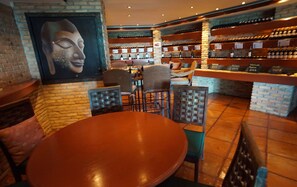 A restaurant interior with brick walls, a mural, tables, chairs, and shelves of wine bottles. - Bougainvillea Terrace House (Karon)