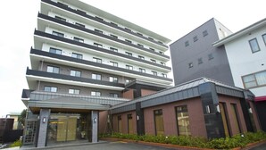 Um hotel de vários andares com design moderno, destacando uma entrada imponente com porta de vidro e área de estacionamento com marcações amarelas.