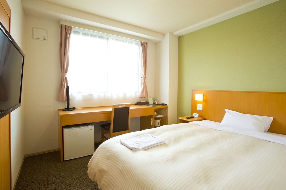 Quarto de hotel com cama, escrivaninha, cadeira e televisão.