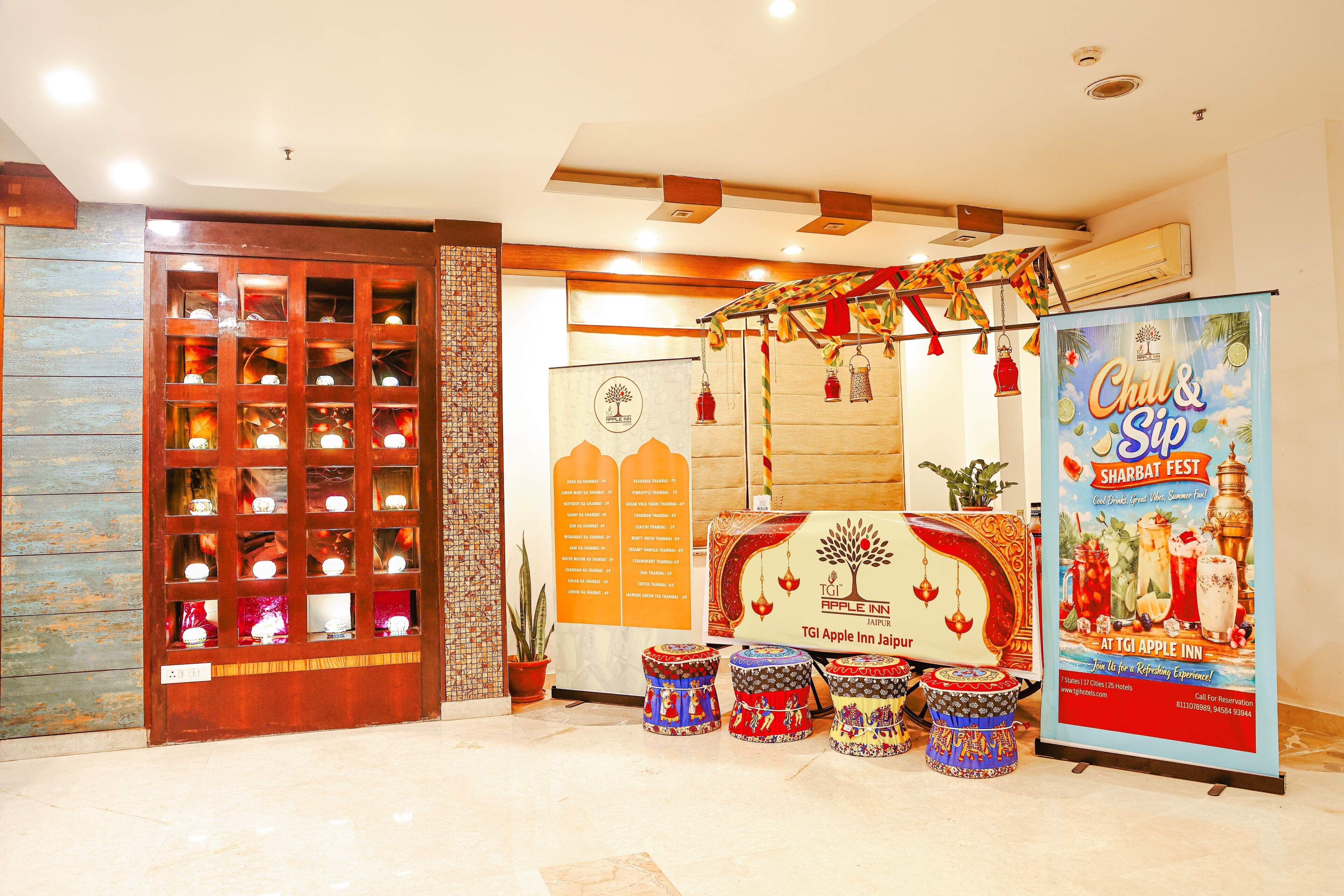Um saguão de hotel com uma vitrine de madeira, um cartaz para um festival de Shabat e banquinhos indianos tradicionais.