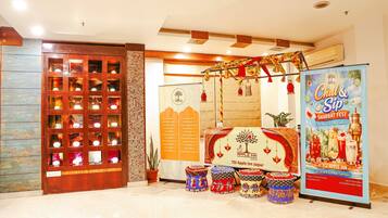 Um saguão de hotel com uma vitrine de madeira, um cartaz para um festival de Shabat e banquinhos indianos tradicionais.
