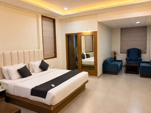 A modern hotel room with a large bed, a seating area with a blue sofa and armchairs, and a mirror reflecting the room. - TGI Apple Inn (Jaipur)