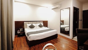 Una habitación de hotel con cama, ventilador de techo, equipo de aire acondicionado, mesita de noche, espejo y puerta.