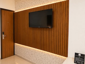 A modern interior with a wooden panel wall, a mounted flat-screen TV, and a door with a keyless lock. - TGI Apple Inn (Jaipur)