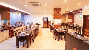 Un comedor de hotel con varias mesas y sillas, una zona de cocina y un mostrador de recepción.