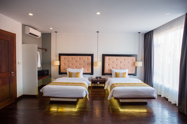 A hotel room with two beds, a wardrobe, an air conditioning unit, and a view of the outdoors.
