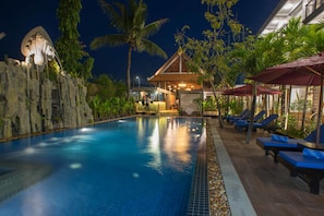 A swimming pool with lounge chairs and umbrellas, surrounded by tropical plants and a rock wall. - Naga Gate Boutique Hotel (Siem Reap)