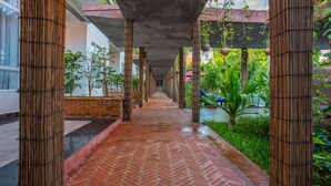 Une allée couverte, avec des colonnes en bambou, un sol en briques et de la verdure.