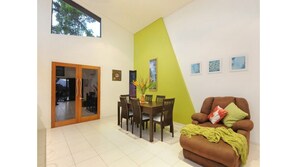 A dining area with a table and chairs, a sofa with a throw blanket, and a green accent wall.