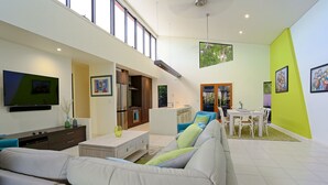 A spacious living area with a sofa, dining table, and kitchen in the background. - Hilltop Views (Cannonvale)