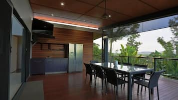 A modern kitchen with wooden paneling, a stainless steel refrigerator, and a glass dining table with chairs.