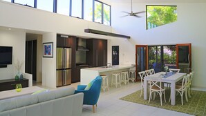 A spacious kitchen with a large island, a dining area with white chairs, and a ceiling fan. - Hilltop Views (Cannonvale)