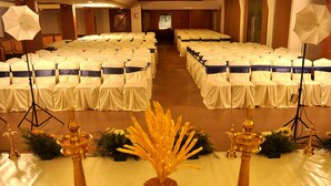 Une salle de banquet avec des rangées de tables recouvertes de nappes blanches et de rubans bleus, décorée de fleurs et de lampes en laiton traditionnelles.