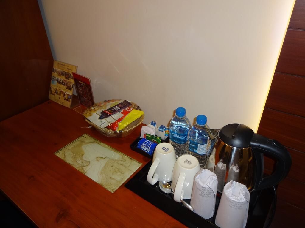 Et hotelværelse med et træbord, en bakke med kaffemaskine, kopper, vand på flaske, en snackpose og en bog.