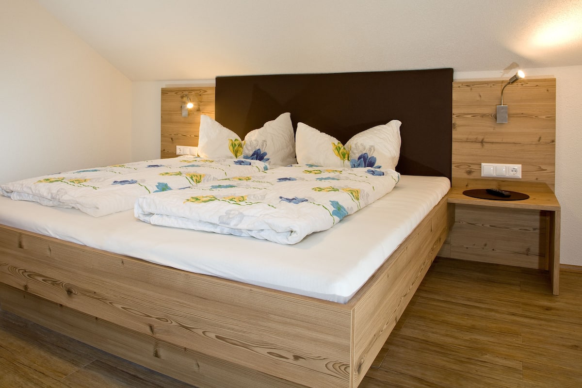 A double bed with a wooden headboard, a bedside table, and a wall-mounted light fixture.