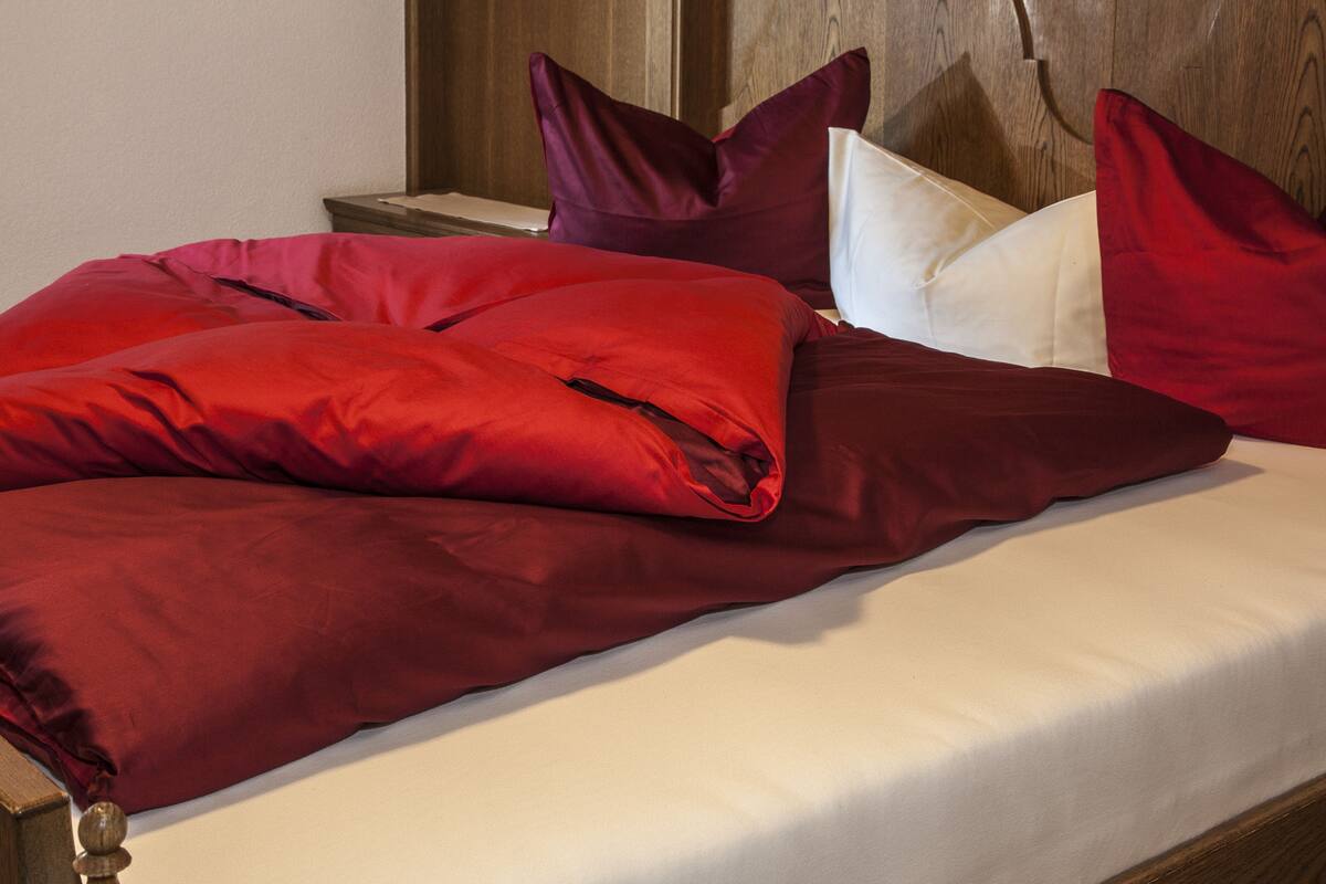 A bed with red and white bedding, wooden headboard, and a nightstand with a lamp.