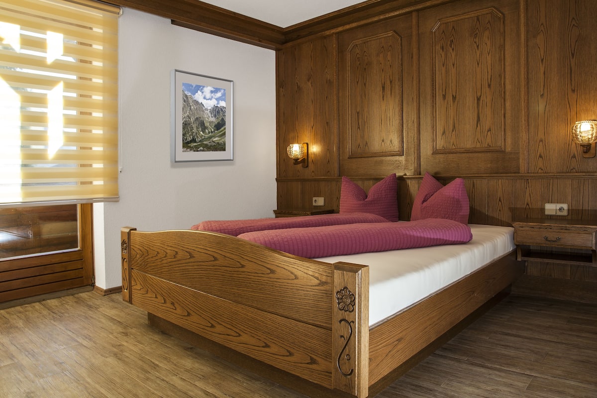 A wooden bed with a headboard, a bedside table, and a wall-mounted light fixture.