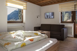 Un dormitorio con cama, sofá, televisor y ventana con vista a la montaña.