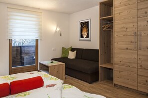 A room with a bed, a sofa, a small table, a wardrobe, and a window with blinds. - Apart Bergland (Kaunertal)