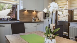 A modern kitchen with white cabinets, a wooden countertop, and a dining area with a table and chairs. - Apart Bergland (Kaunertal)