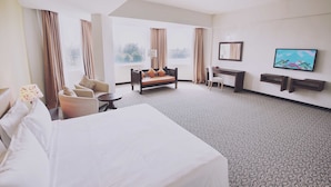 A hotel room with a large bed, a sofa, a desk, and a TV. There are curtains on the windows, and a lamp is on the desk. - The Regency Waterfront Hotel (Kuala Terengganu)