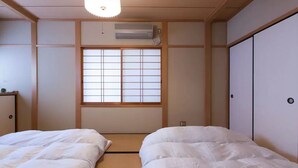 A traditional Japanese room with tatami flooring, a shoji screen window, and a bed with white bedding.