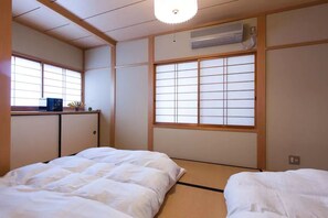 Et traditionelt japansk værelse med tatamimåtter, et shoji-skærmvindue og en seng med hvidt sengetøj.