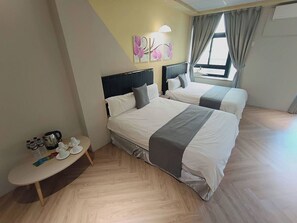 A hotel room with two beds, a small table with a kettle and cups, and a window with curtains.