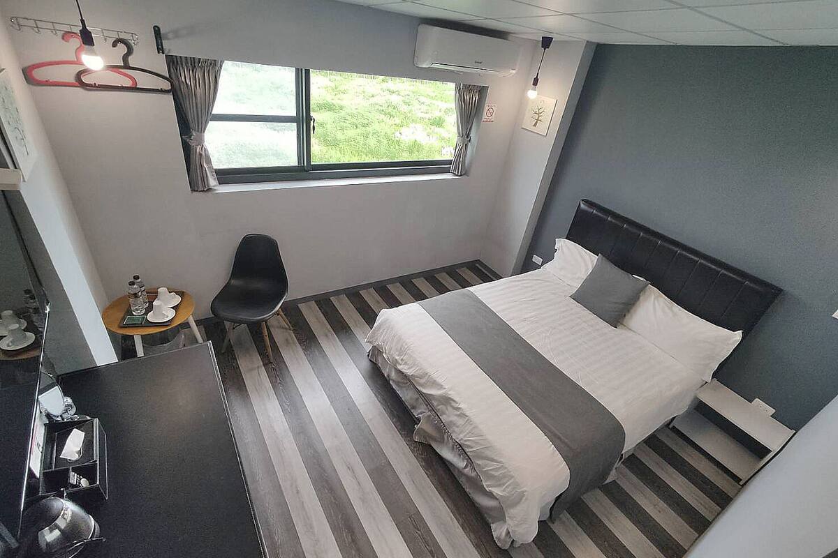 Ein Hotelzimmer mit Bett, Schreibtisch, Stuhl, einem Fenster mit Vorhängen und Blick auf Grünfläche.