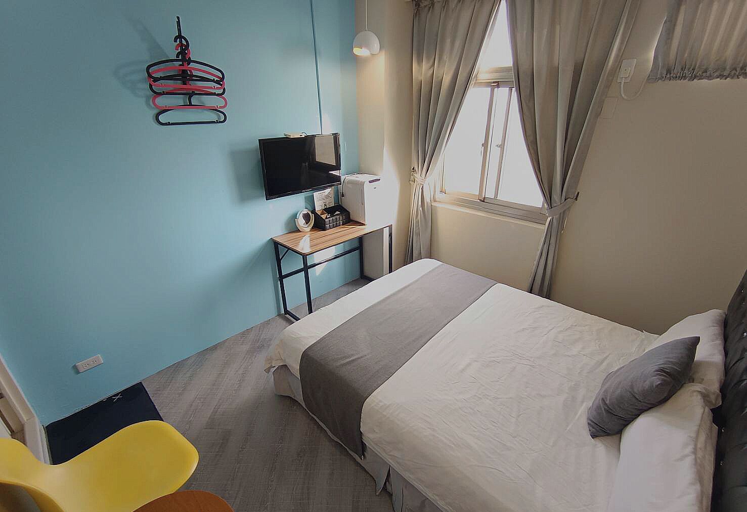 A hotel room with a bed, a desk with a computer, a chair, and a window with curtains.