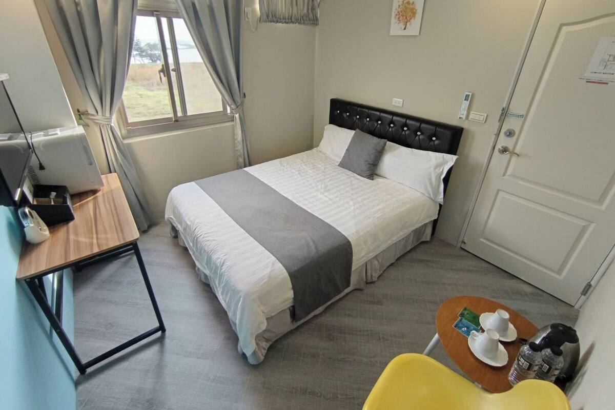 Ein Hotelzimmer mit einem Bett, einem Schreibtisch mit Computer, einem Stuhl und einem kleinen Tisch mit Tassen und einer Flasche.
