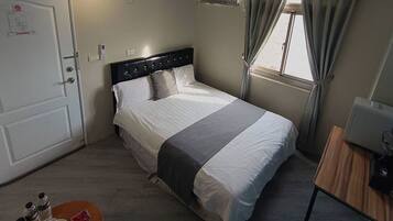 Un dormitorio con cama, escritorio, silla, ventana y puerta.